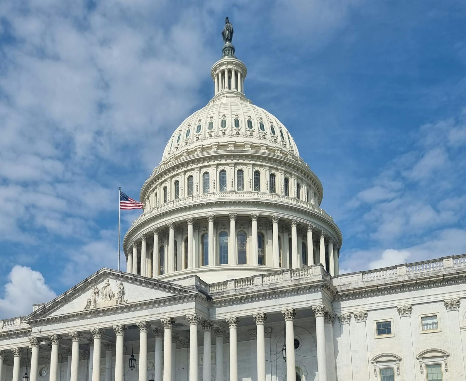 A striking view of the US Capitol dome with flag and blue sky in Washington, DC.